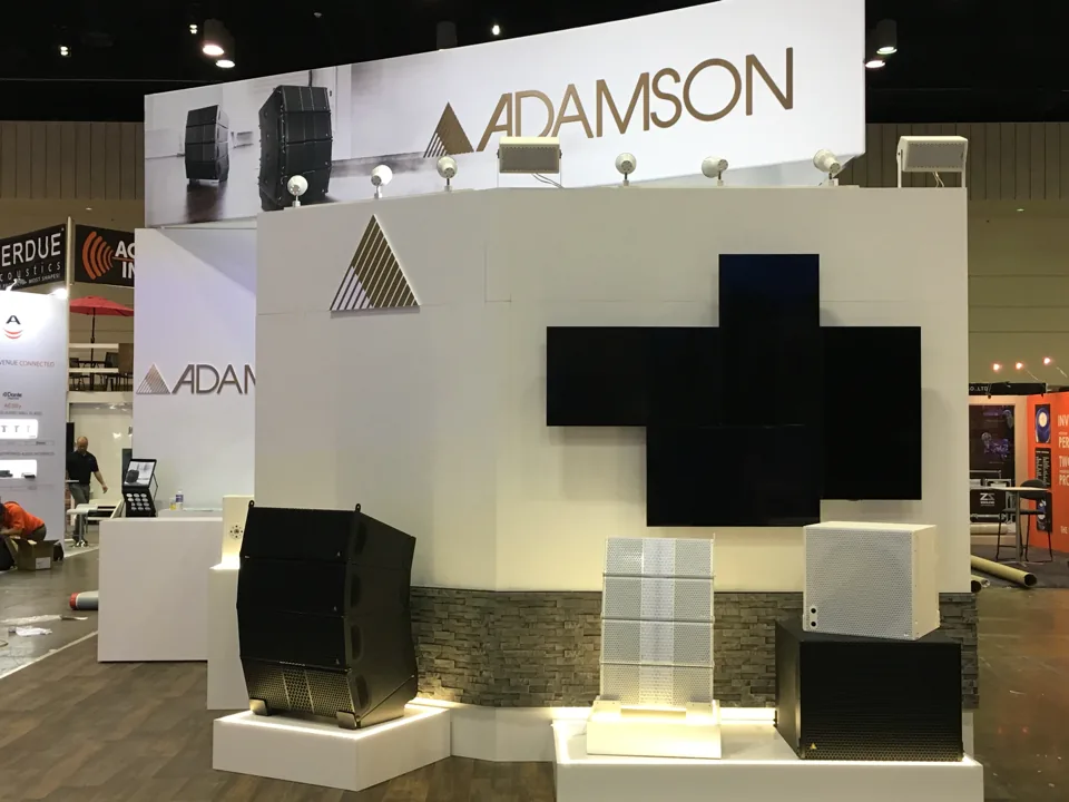 Adamson exhibit with a stone plinth wall, mounted speakers and a cross of displays