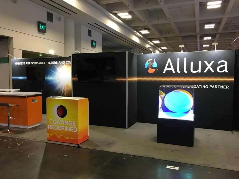 Alluxa exhibit with a dark backlit wall and illuminated product plinth