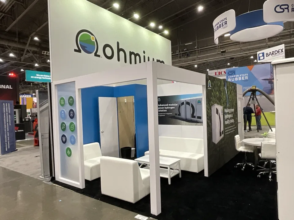 Ohmium exhibit with green hydrogen graphics and white meeting pods